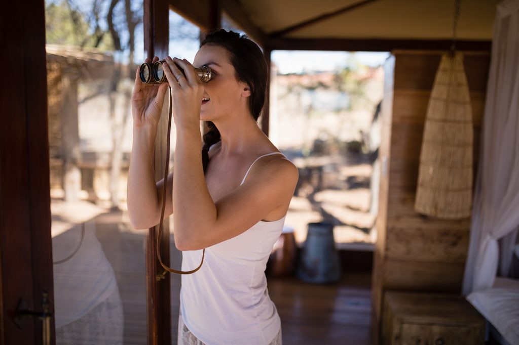beautiful woman looking through binoculars from window during safari vacation